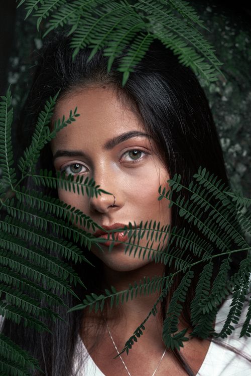 Free Close-up portrait of a woman behind green fern leaves, portraying natural beauty. Stock Photo