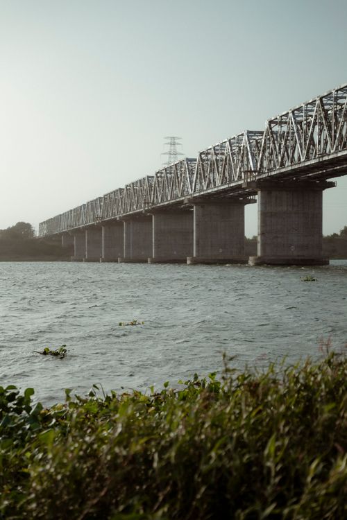 Free A scenic view of a steel bridge crossing a tranquil river under a clear sky. Stock Photo