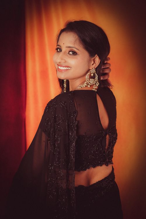 Free A woman in a stylish black saree posing gracefully against a warm backdrop. Stock Photo