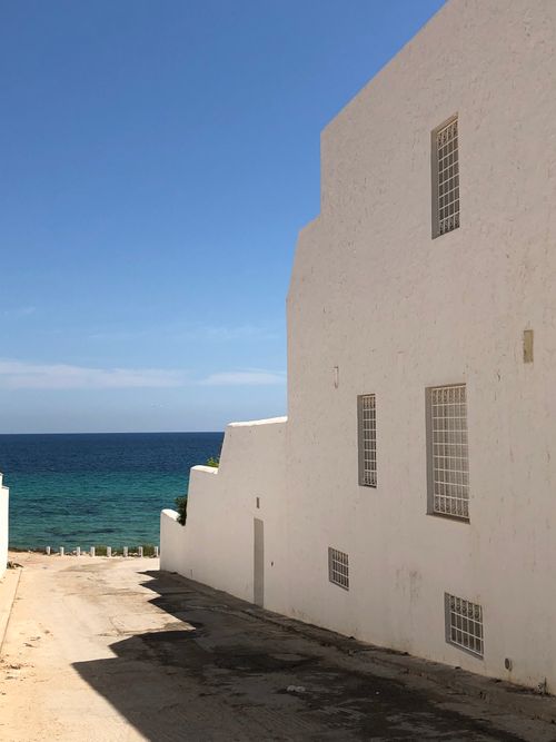 Free A serene coastal building with white walls facing the calm blue ocean under a clear sky. Stock Photo
