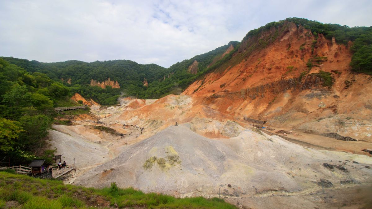 Orange and white volcanic slopes of Noboribetsu Jigokudani surrounded by green forest in summer