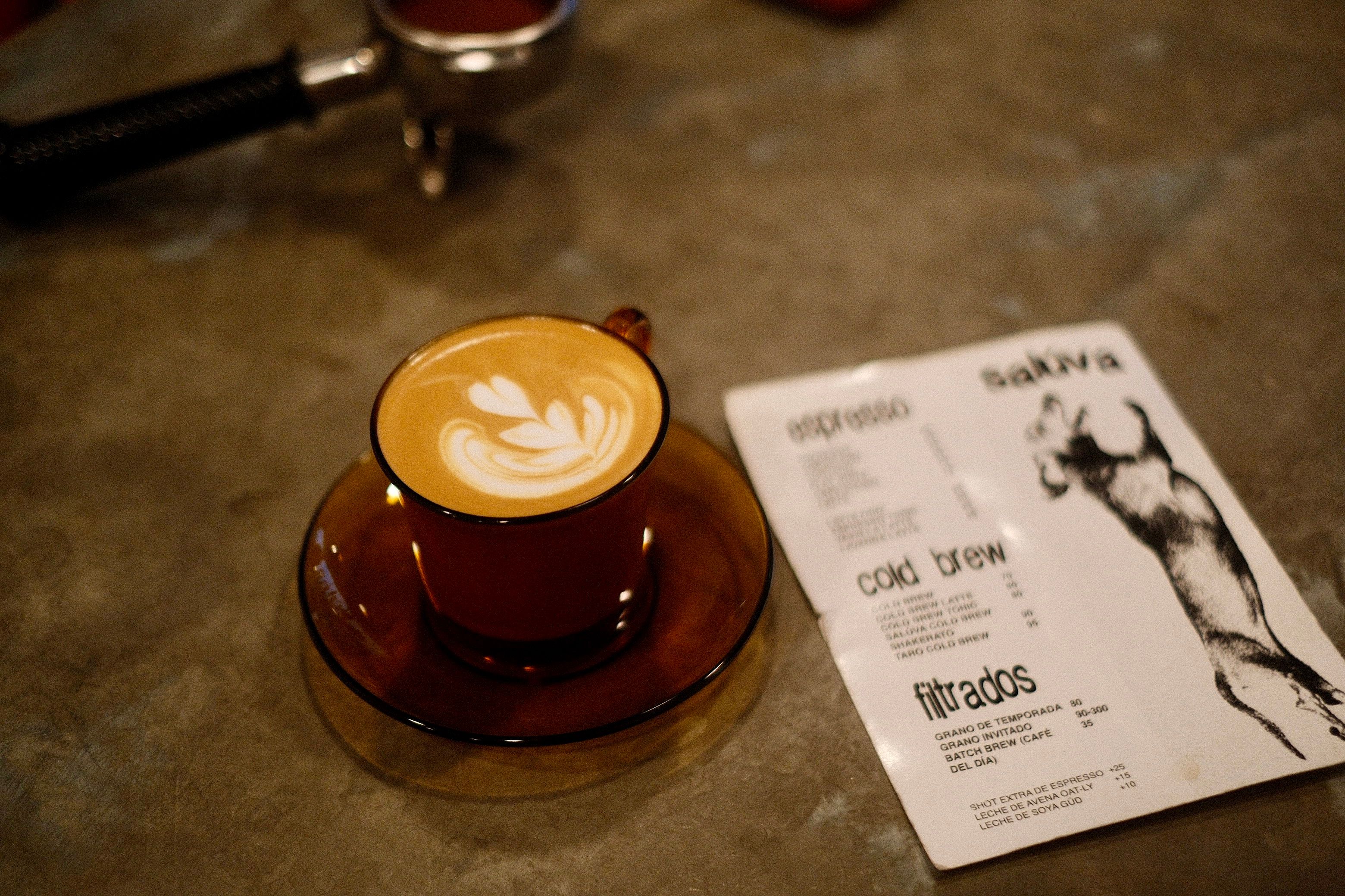 A warm cup of latte with beautiful latte art beside an espresso menu on a rustic table.