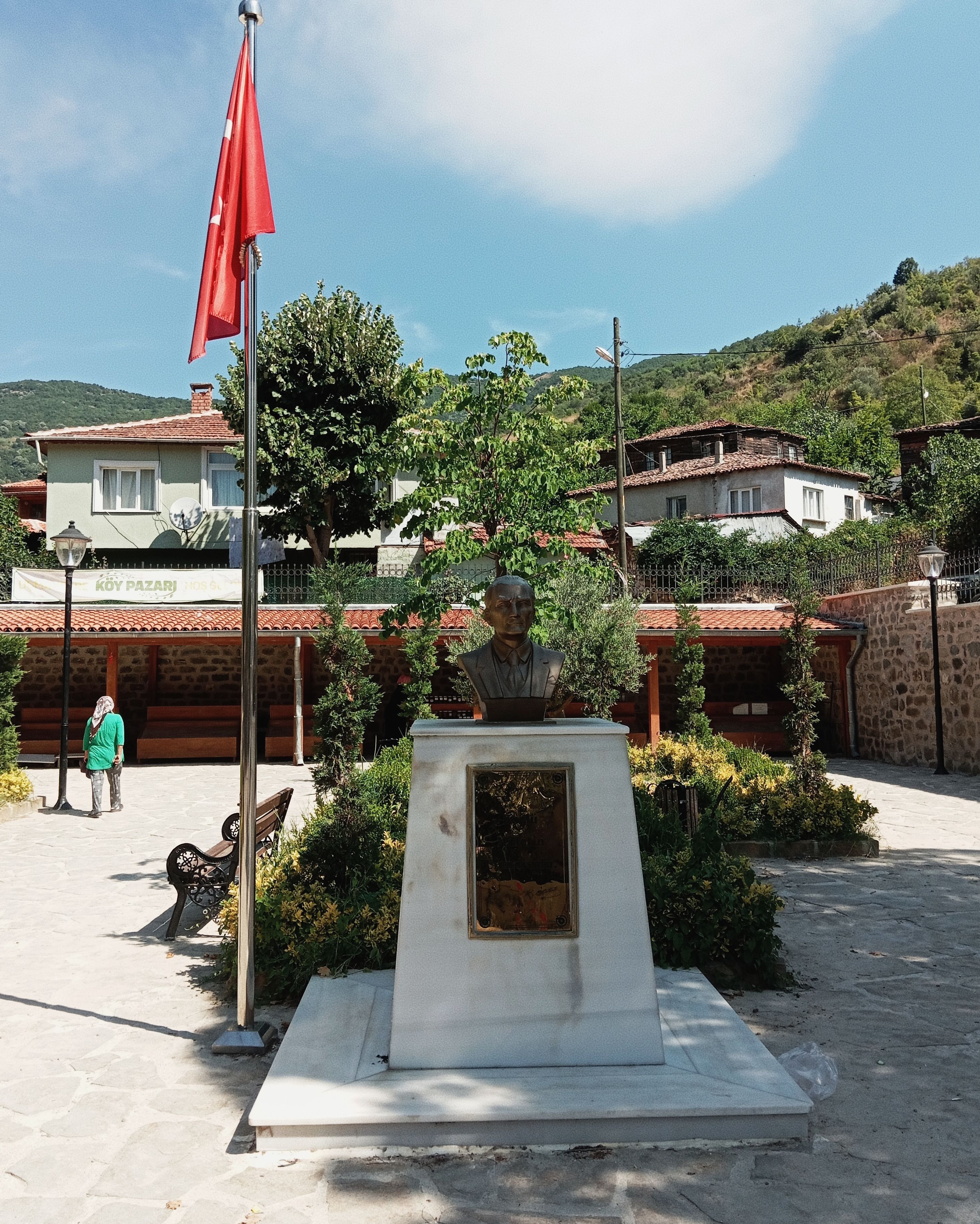 A scenic view of a bust monument in a Tekirdağ square, framed by greenery and a Turkish flag.