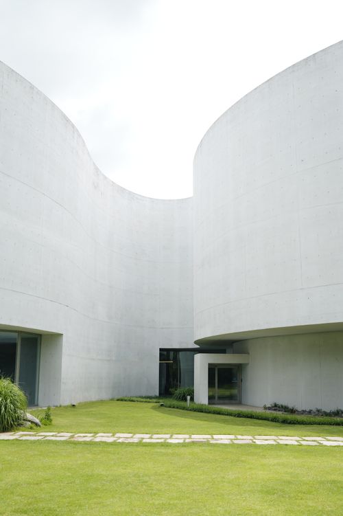Free Stunning modern architecture featuring minimalist concrete curves and a serene garden area. Stock Photo