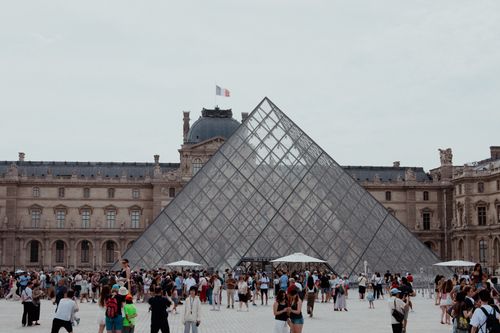 Free A bustling scene at the Louvre Pyramid in Paris with tourists exploring the iconic landmark. Stock Photo