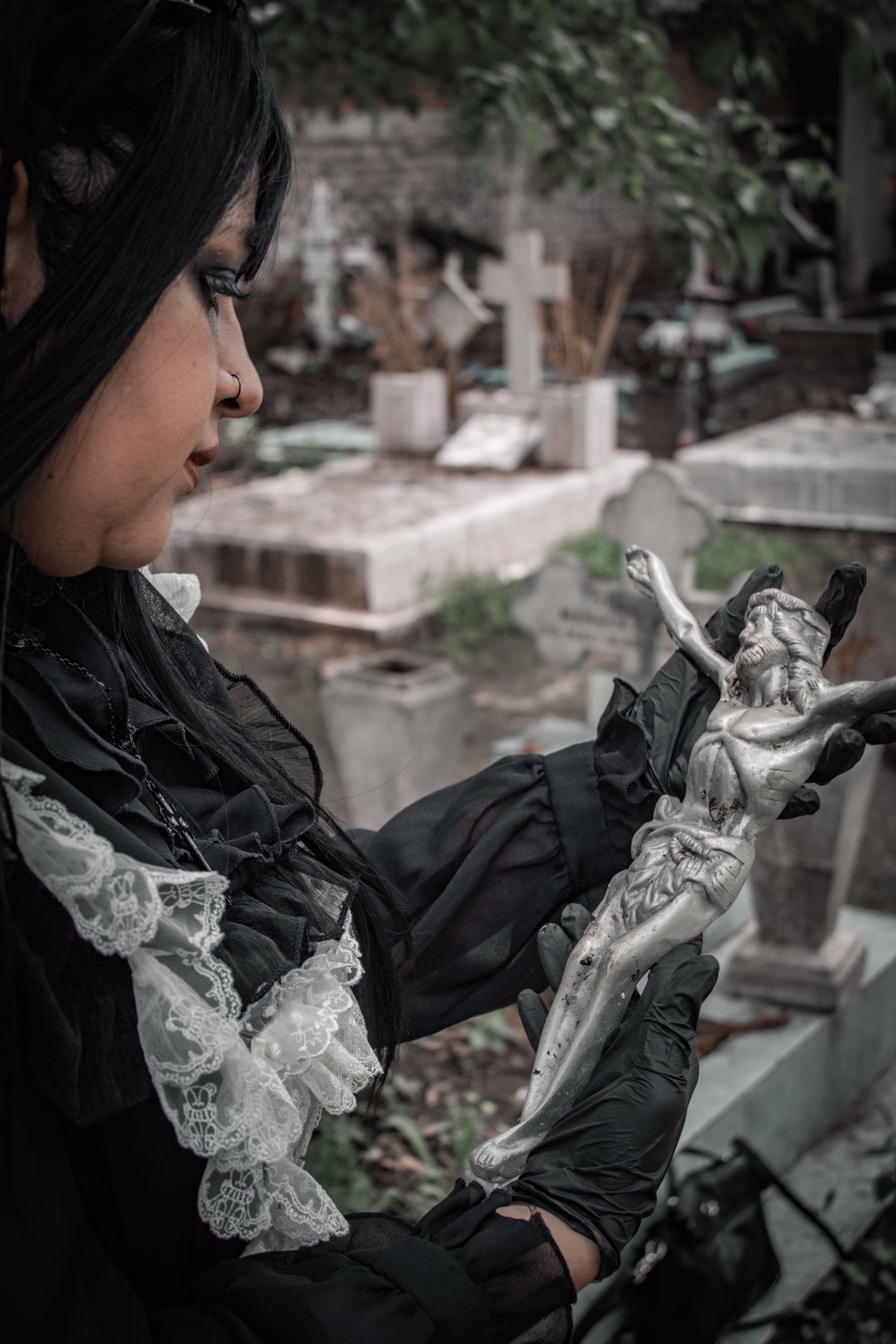 A gothic woman holding a silver crucifix in an atmospheric cemetery in Mexico City.