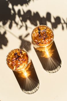 Beautiful herbal tea with floral garnish in elegant glasses, casting unique shadows in warm sunlight.