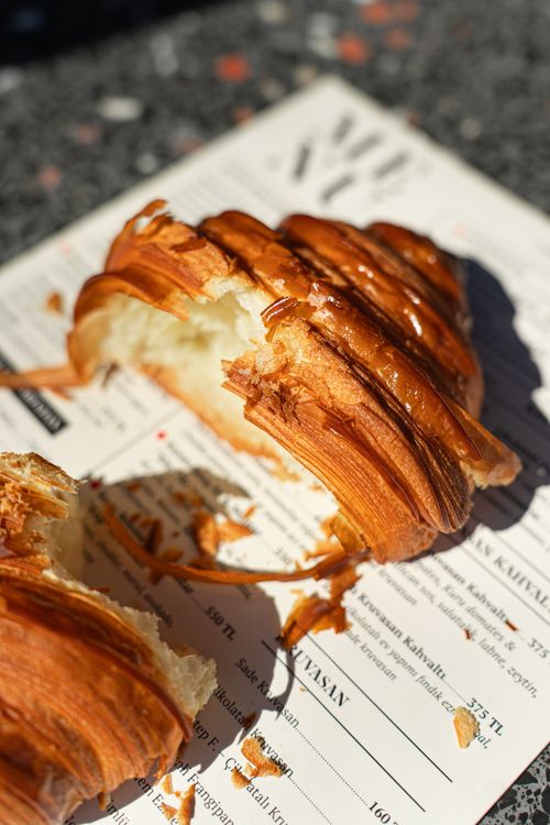 Free Close-up of a freshly baked croissant on a cafe table in sunlight, with flaky crust details. Stock Photo