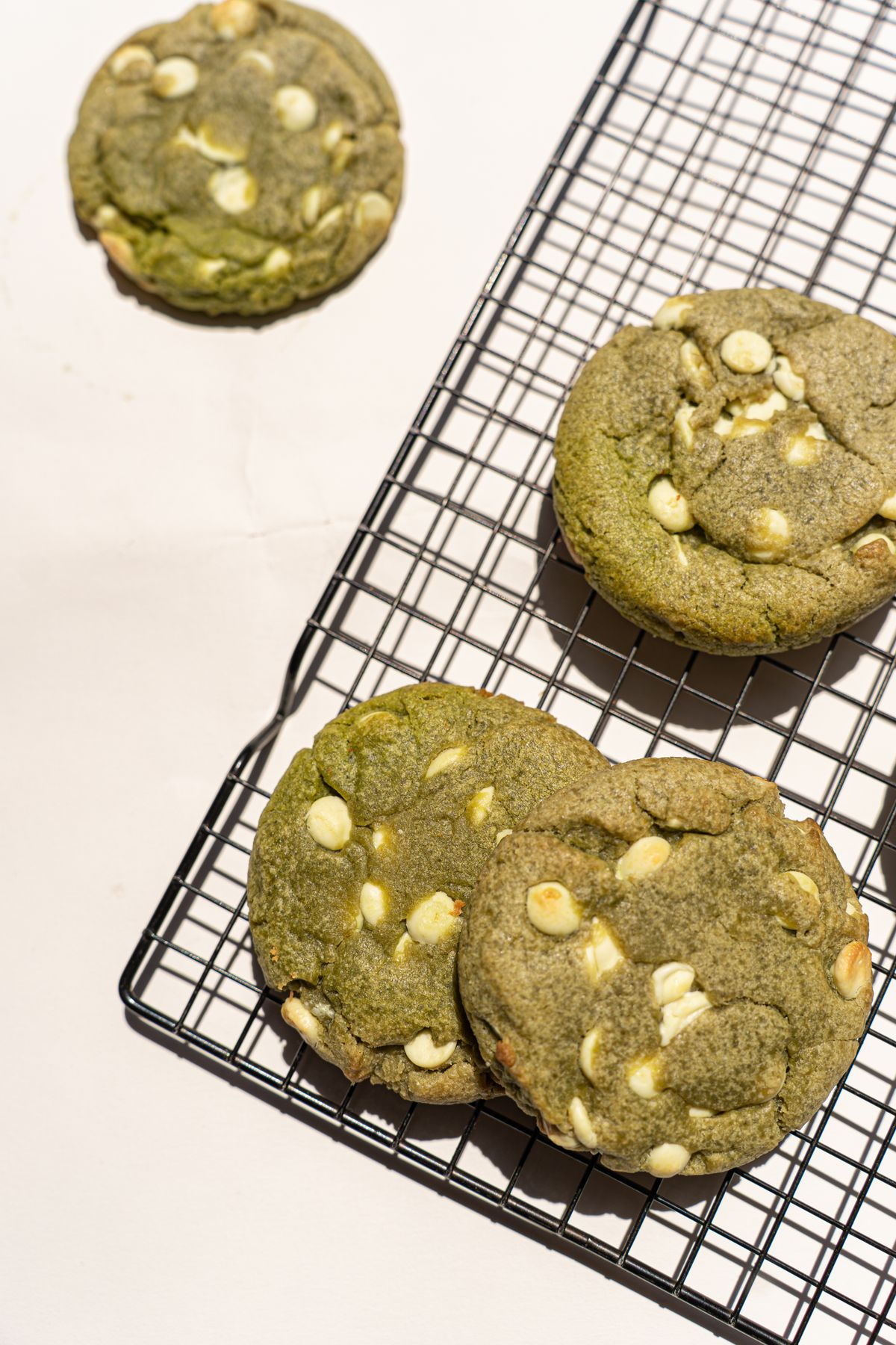 Green cookies with white chocolate chips cooling on a black wire rack