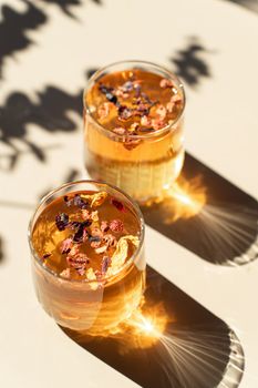 Two glasses of herbal tea adorned with dried flowers, casting artistic shadows.