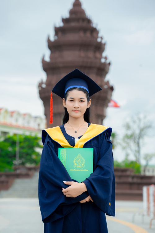 Free Young adult in cap and gown celebrating graduation in front of a Cambodian monument. Stock Photo