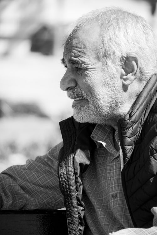 Free A contemplative senior man with gray hair and a beard sitting outside, captured in black and white. Stock Photo