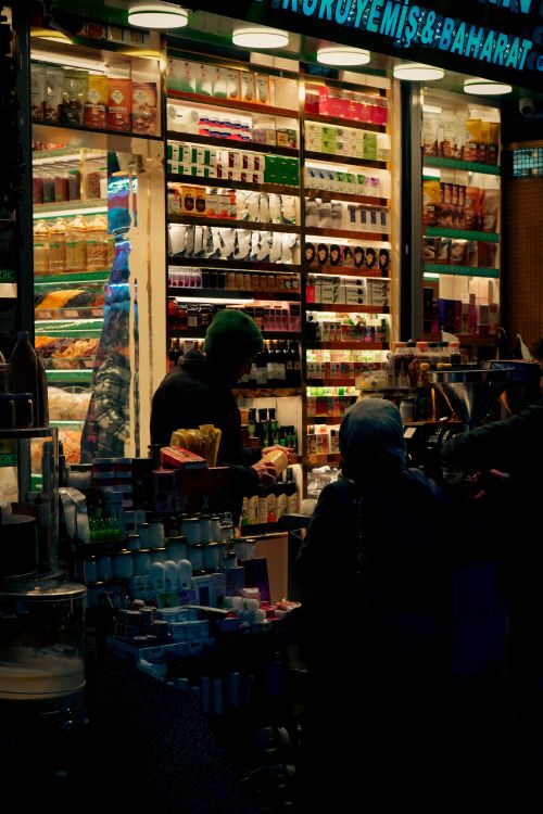 Free A bustling spice stall at a night market with colorful packaging and two shoppers. Stock Photo