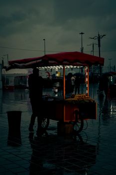 Silhouette of a street vendor with a cart in a rainy, moody urban setting at night.