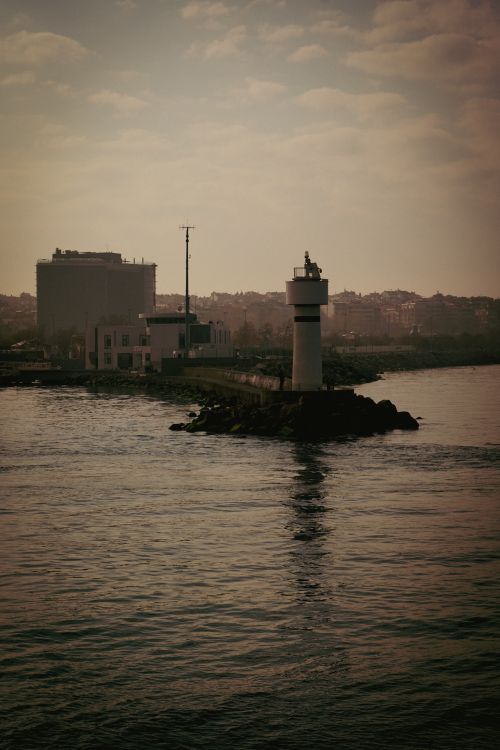 Free Lighthouse stands tall in a serene misty harbor at dusk, creating a calm coastal scene. Stock Photo