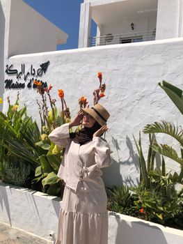 Woman in sun hat poses by vibrant garden at Maison de Jasmine.