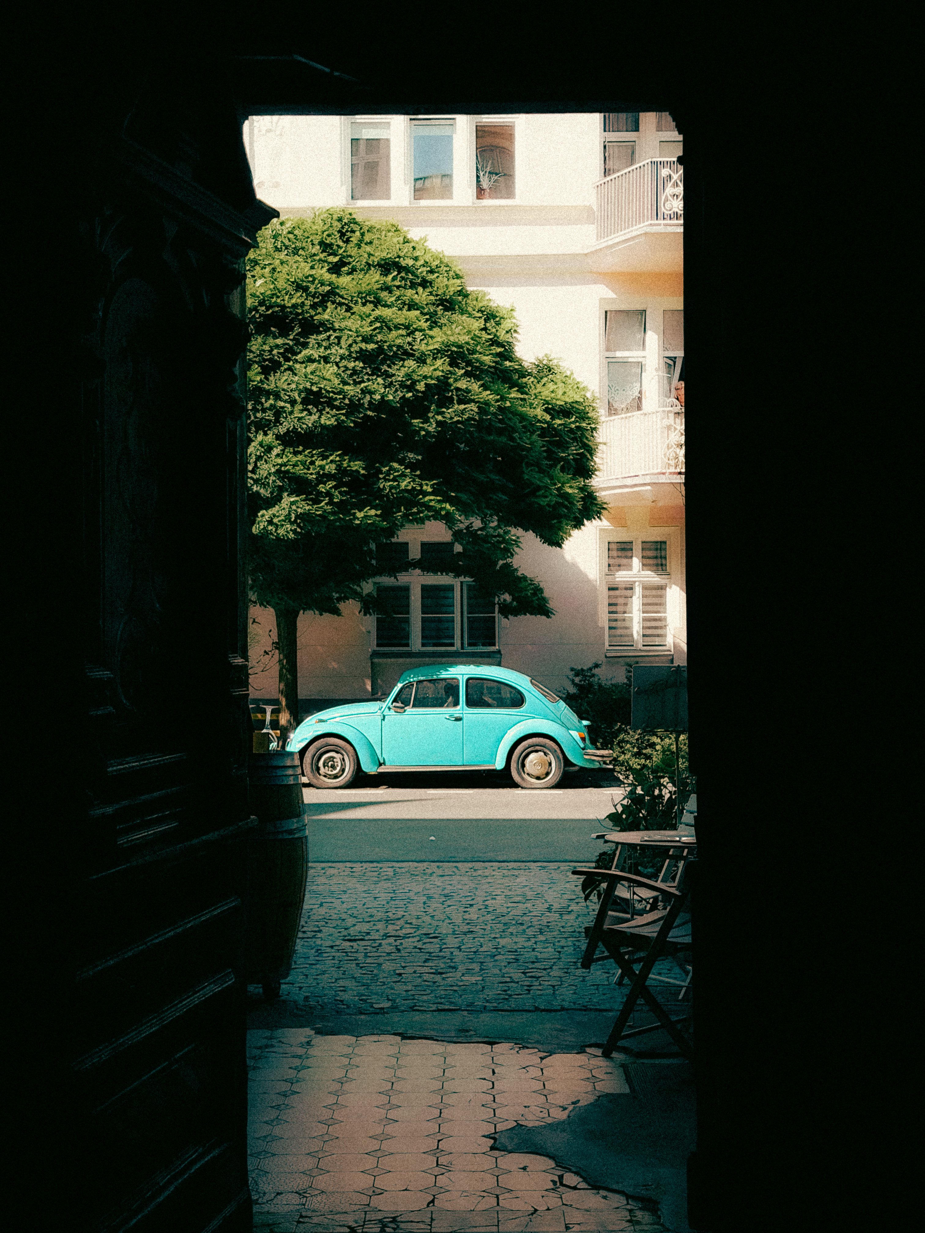 A classic blue car seen through a doorway in a city street scene.