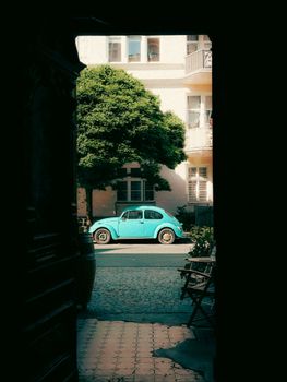 A classic blue car seen through a doorway in a city street scene.