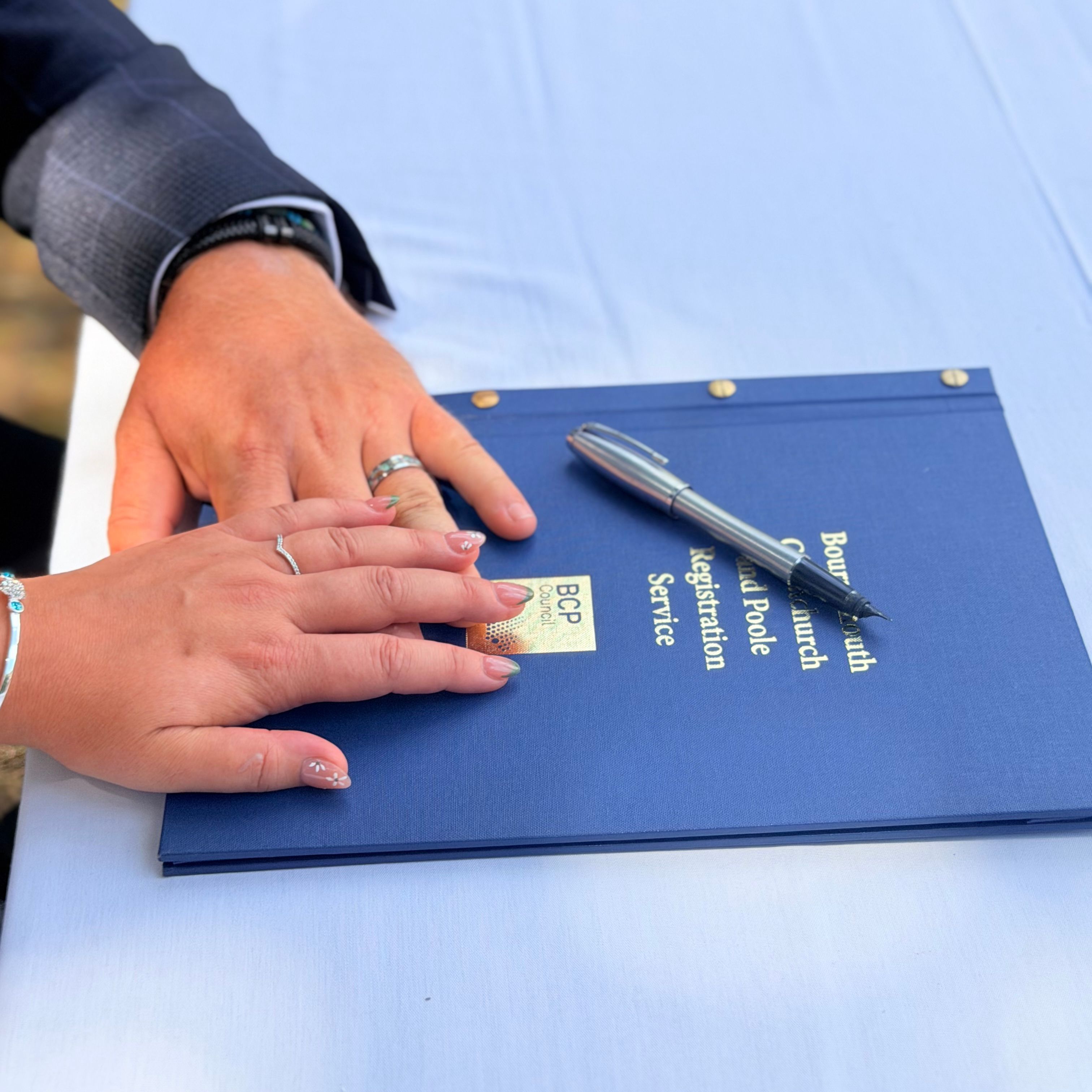 Couple's hands on a wedding registration folder with a pen outside.