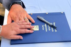 Couple's hands on a wedding registration folder with a pen outside.