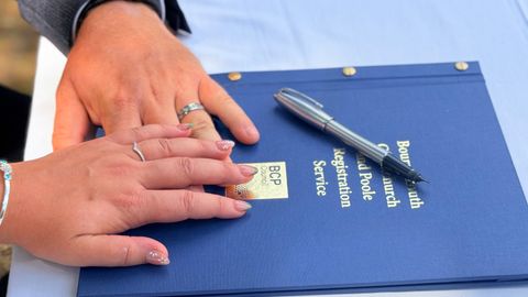 Couple's hands on a wedding registration folder with a pen outside.