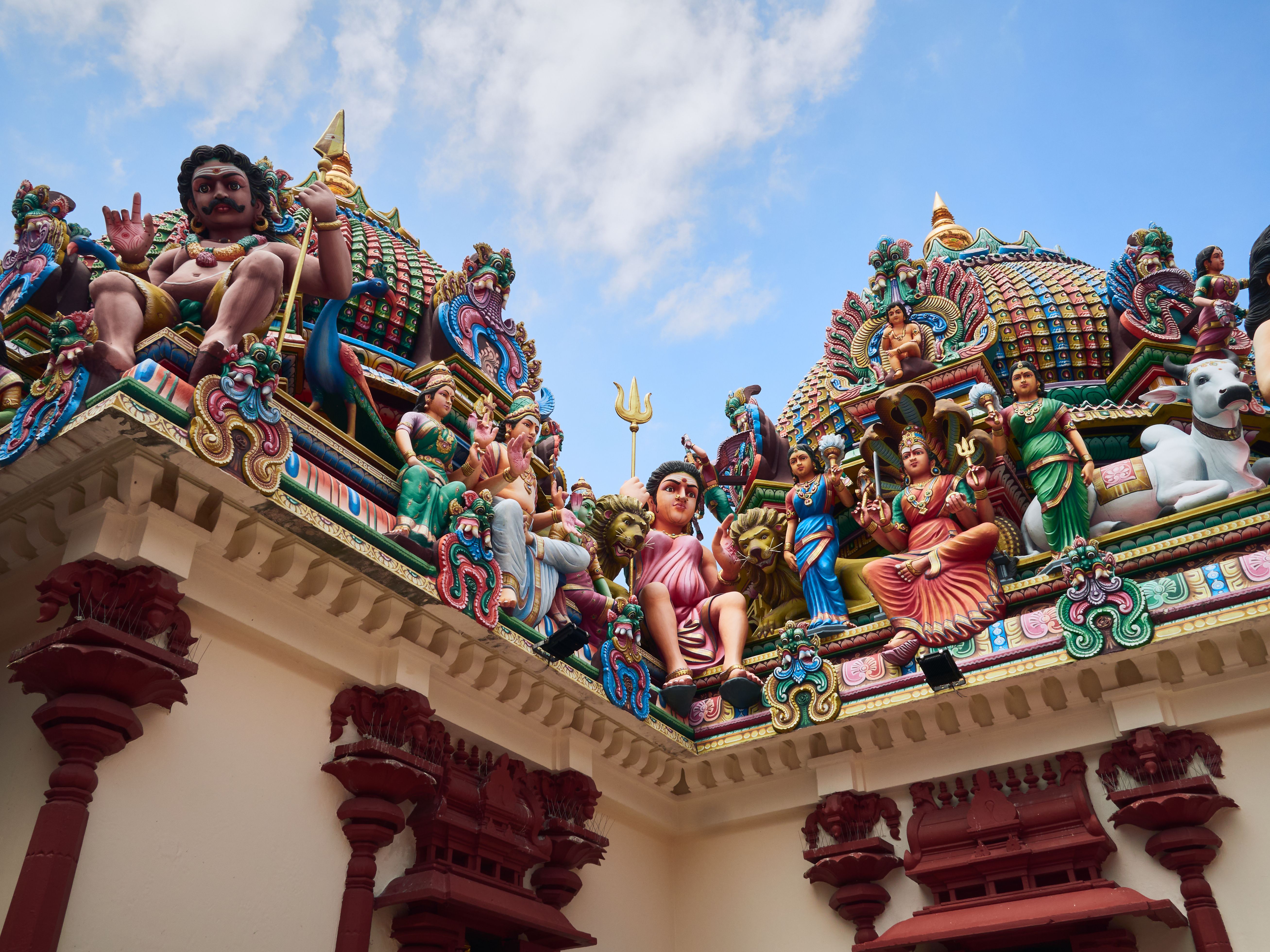Vibrant sculptures adorn a Hindu temple roof under a blue sky, showcasing cultural artistry.