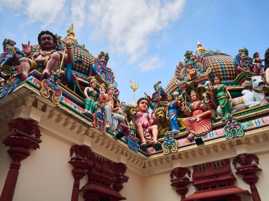 Vibrant sculptures adorn a Hindu temple roof under a blue sky, showcasing cultural artistry.