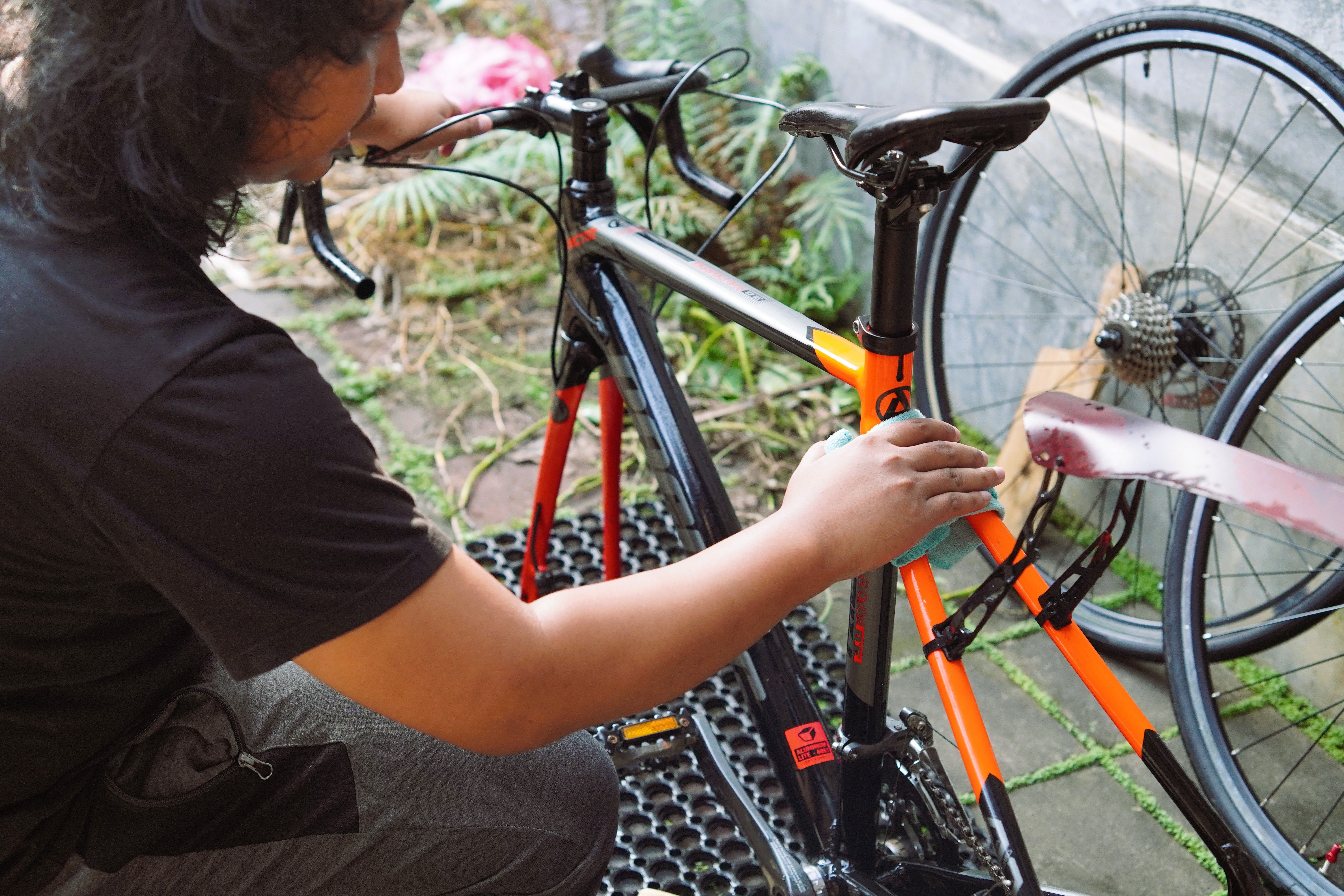 A person cleans a bicycle outdoors, focusing on maintenance and care for the bike.