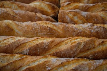 Rows of golden scored baguettes with crackly floured crusts stacked side by side