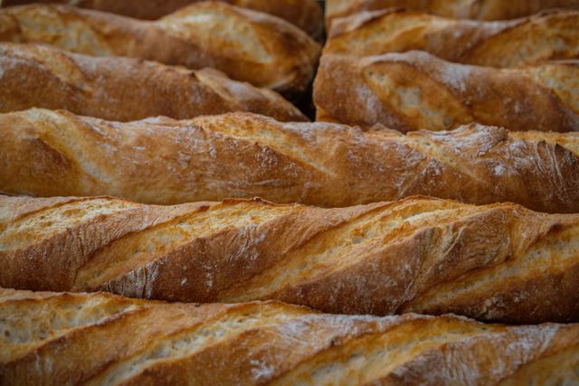 Rows of golden scored baguettes with crackly floured crusts stacked side by side