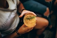 From above of anonymous man in casual clothes sitting in chair and drinking cocktail in glass decorated rosemary while resting with friends