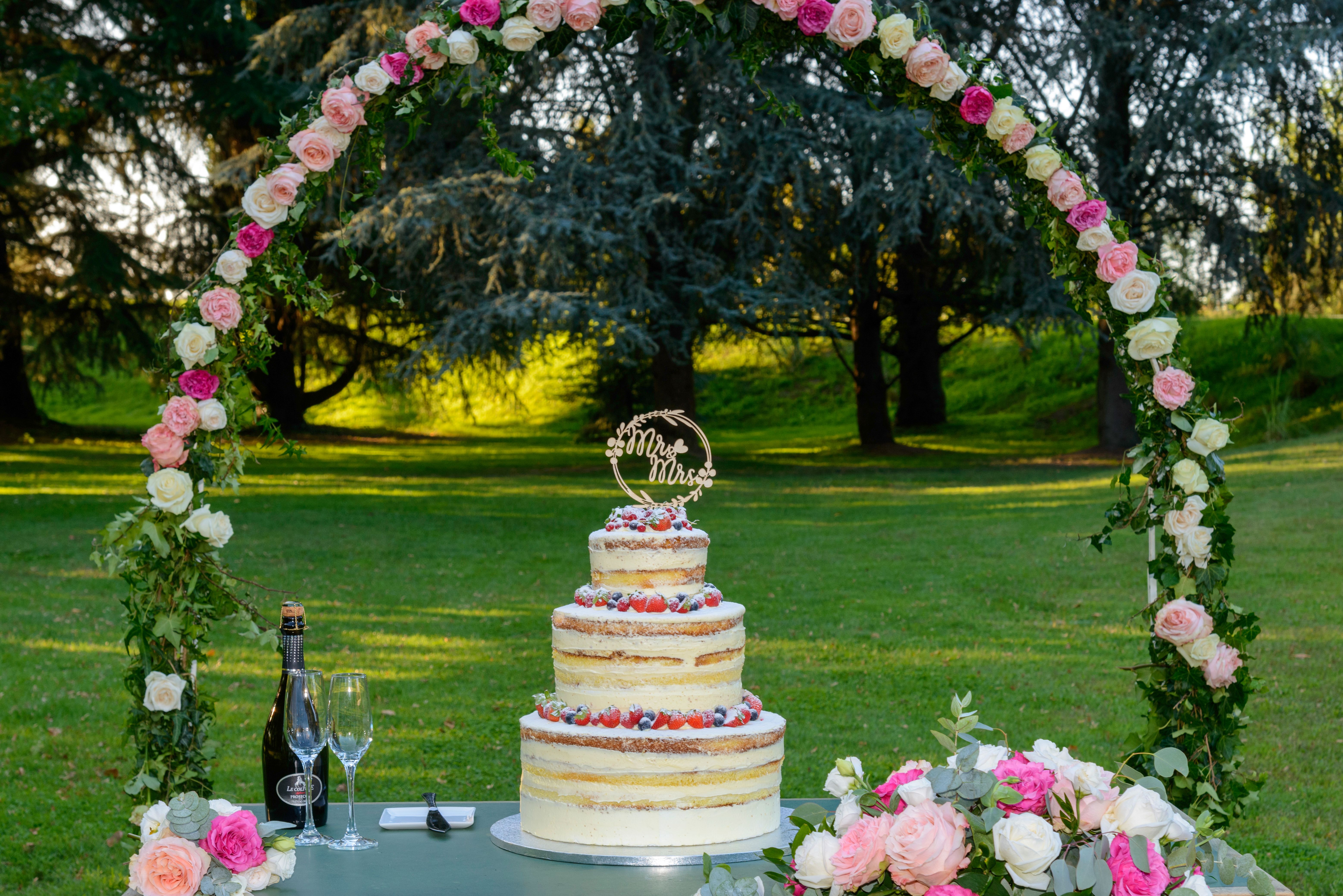A beautiful outdoor wedding cake setup with a floral arch and champagne ready.