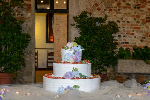 Free Three-tier wedding cake adorned with fresh flowers and strawberries, set in a rustic indoor venue. Stock Photo