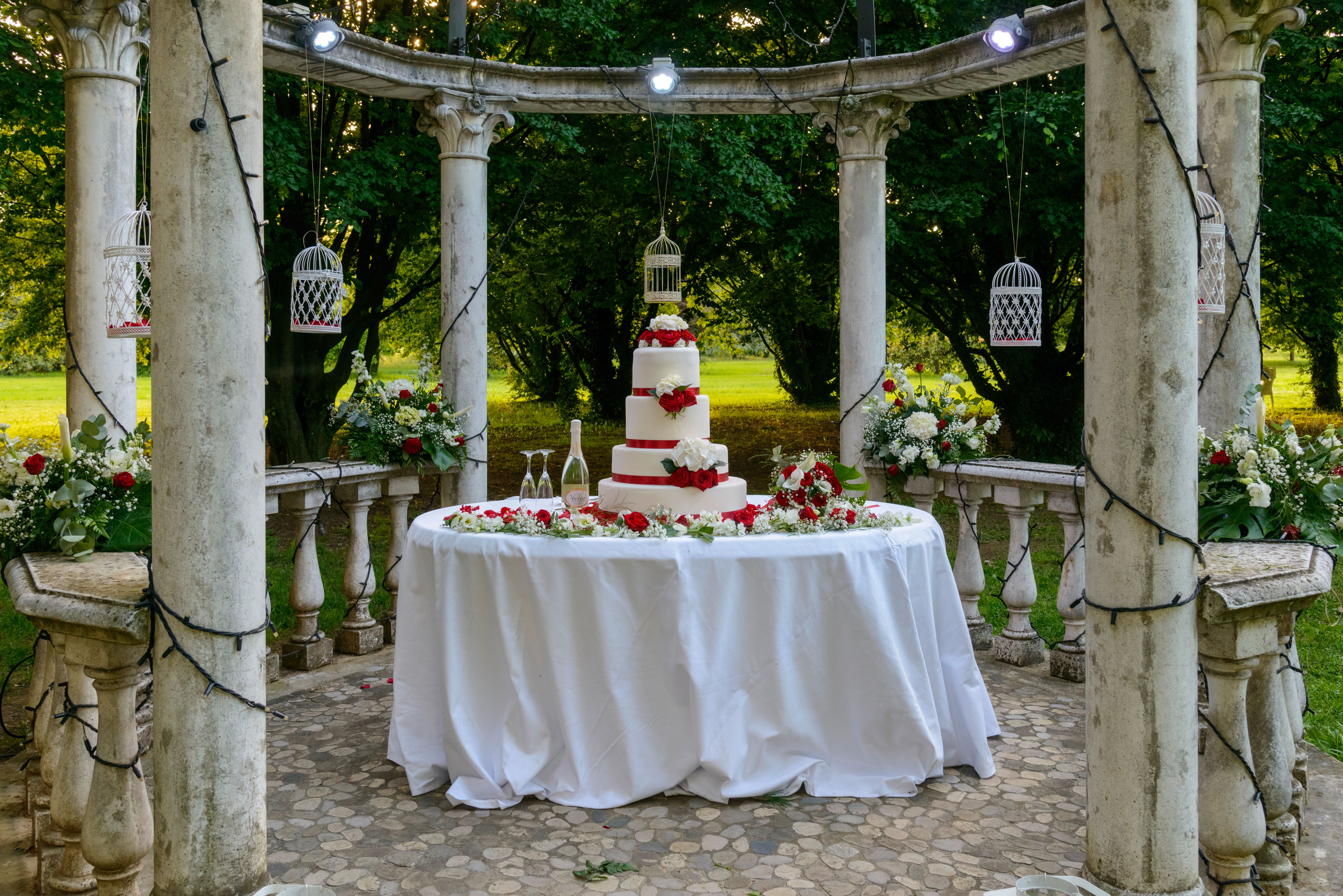 Kue pengantin bertingkat elegan dengan mawar merah di lokasi luar ruangan yang indah.