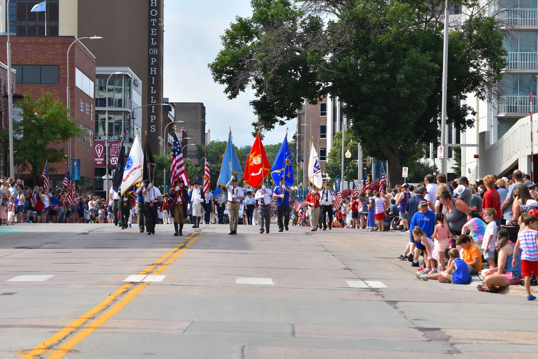 Door hanger delivery in Sioux Falls, SD Door hanger distribution and flyer delivery in Sioux Falls, SD — A festive parade with colorful flags and spectators in a city center street scene. above neighborhoods DoorBlitz crews walk