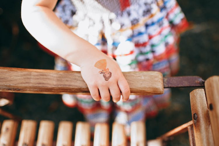 Crop Kid With Tattoo Sticker Standing Near Wooden Bench