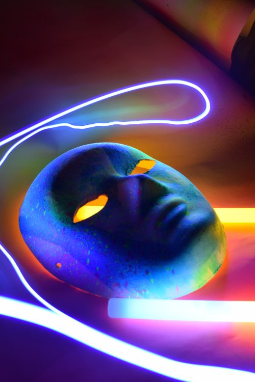 Free Abstract art featuring a vibrant mask illuminated by neon light trails in a dark setting. Stock Photo