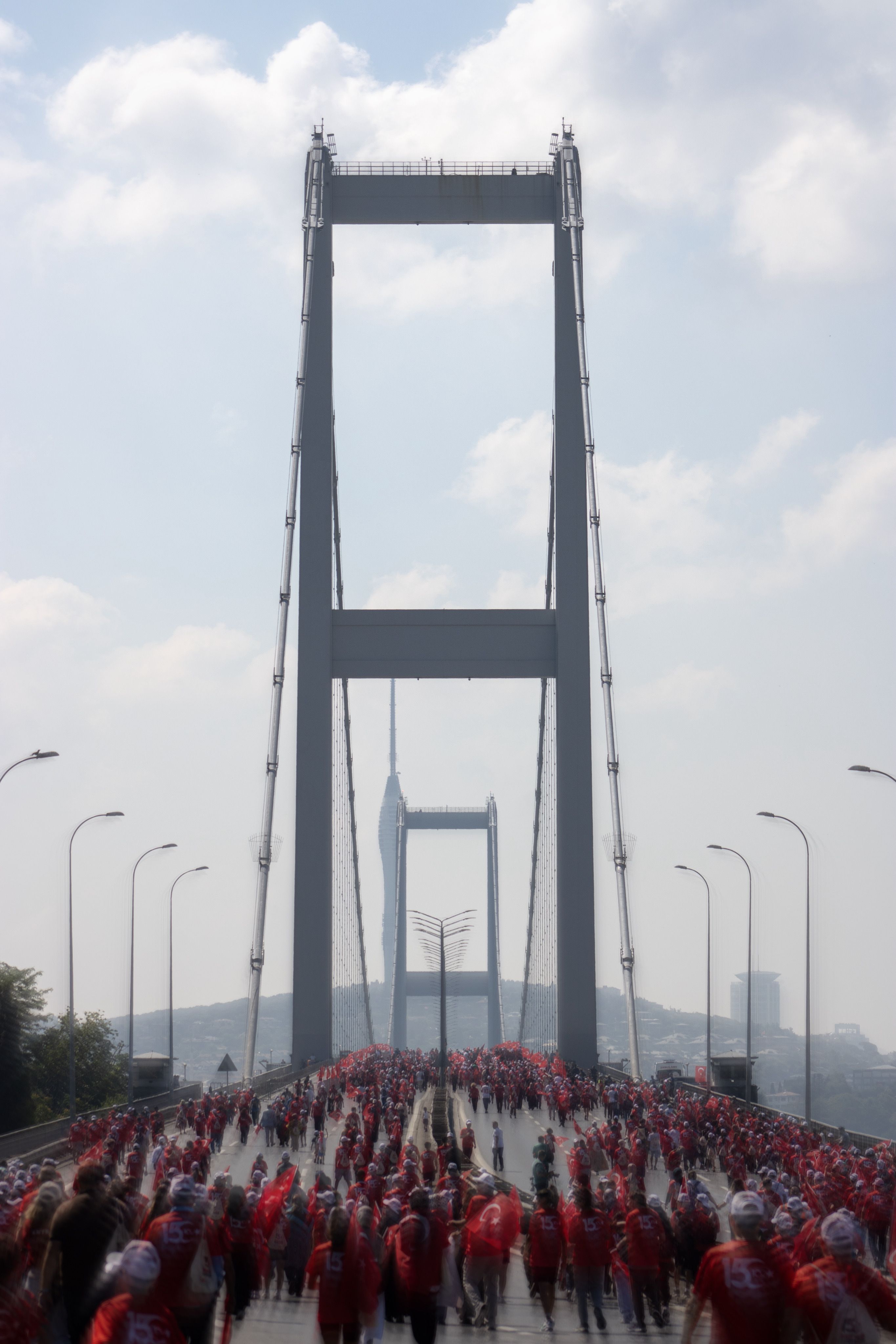 A large group of people crossing a famous bridge in İstanbul under a clear sky.