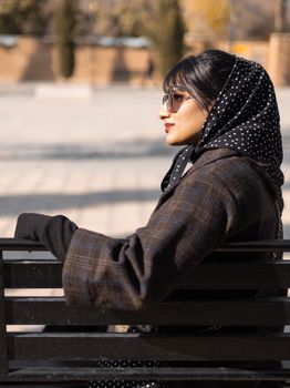 Fashionable woman in sunglasses sitting on a park bench in Berlin, Germany