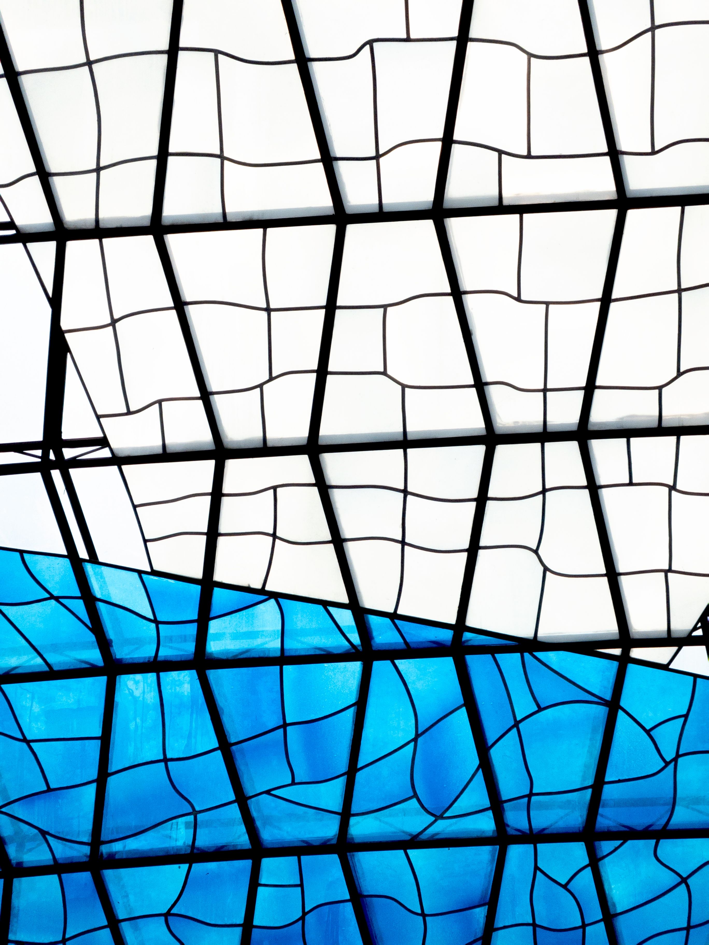 Abstract view of a stained glass ceiling with geometric patterns in Brasília, DF, capturing blue and white hues.
