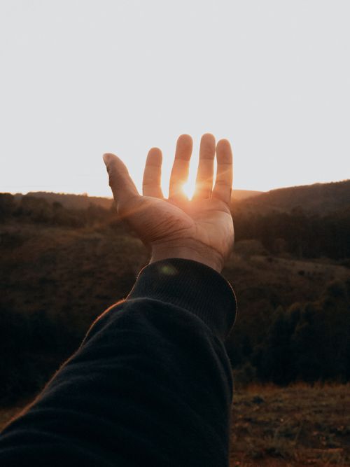 Free A peaceful view of a hand reaching towards the setting sun over a hilly landscape in MG, Brazil. Stock Photo
