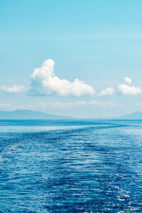 Free A calm ocean under a clear blue sky with fluffy clouds on a bright summer day. Stock Photo