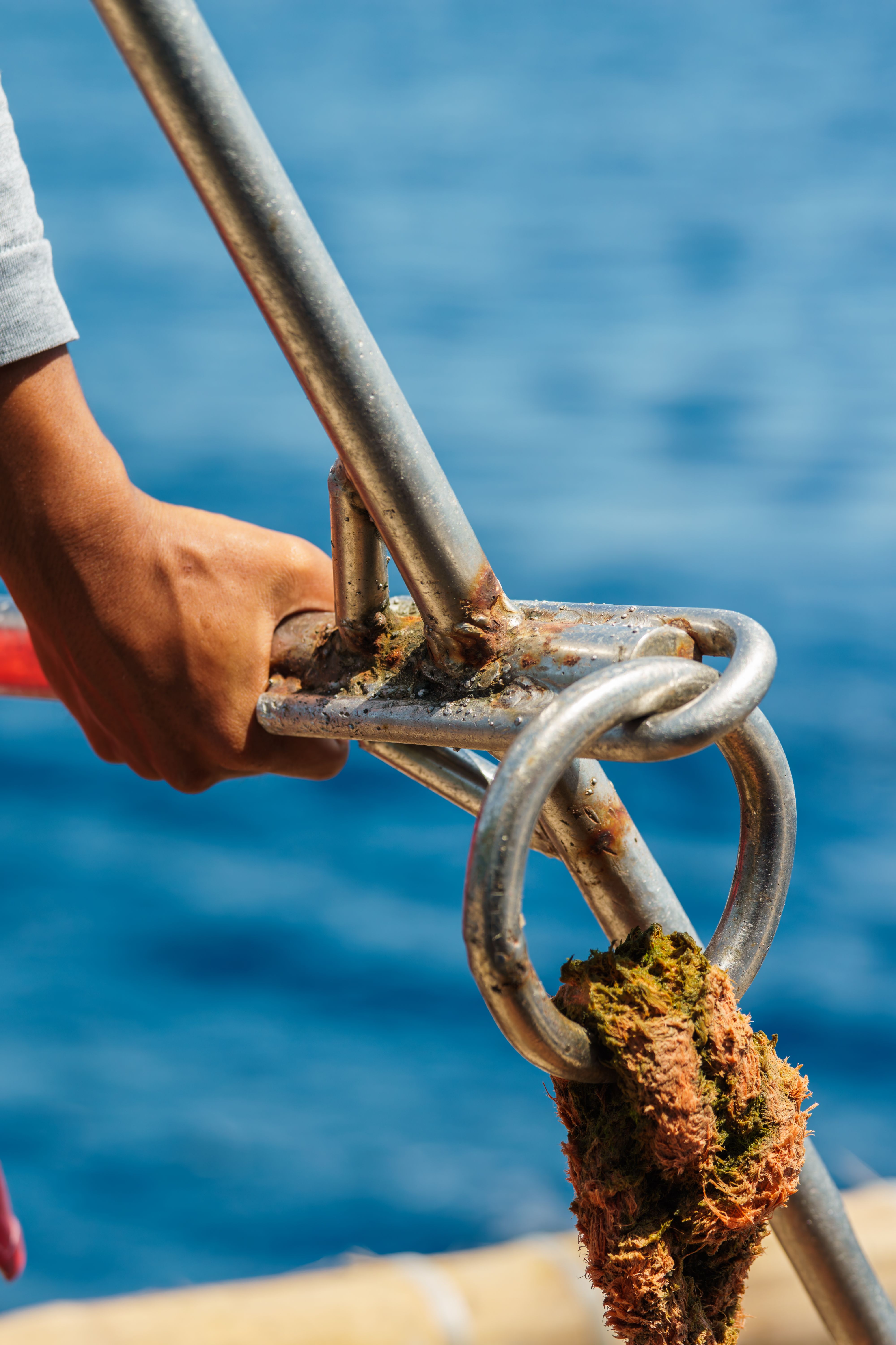 Close-up of a person's hand holding a boat anchor chain with blue ocean background.