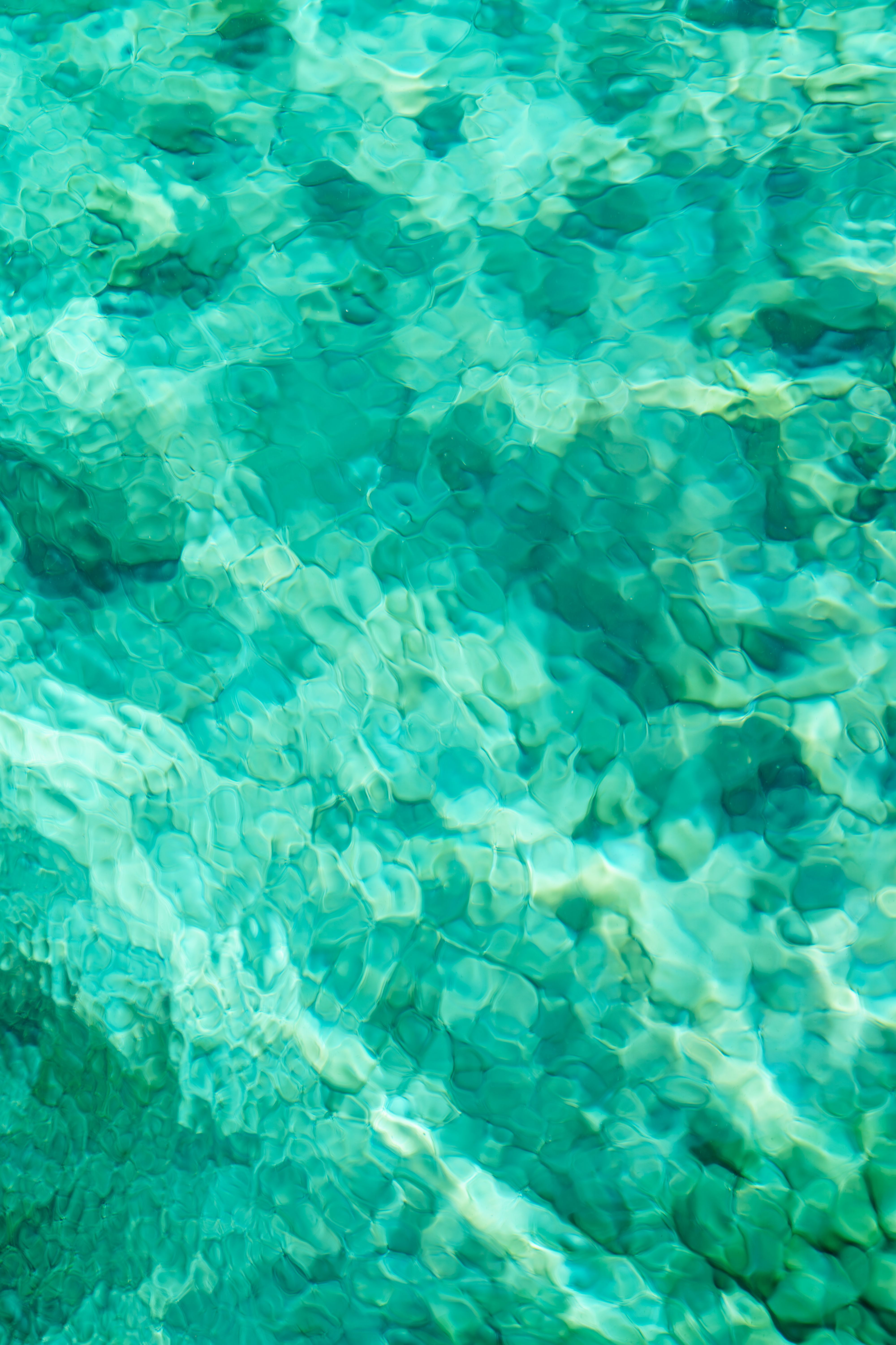 Close-up of clear turquoise water with abstract patterns and vibrant shades of green.