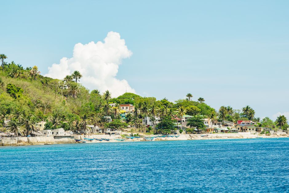 A picturesque coastal village surrounded by lush greenery and clear blue waters under a bright sky.