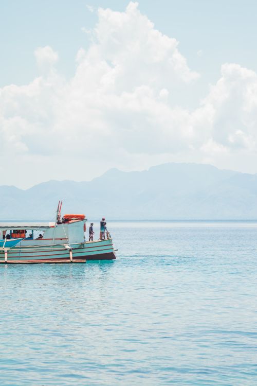 Free A boat glides through clear tropical waters under a bright sky, offering a serene escape into nature. Stock Photo