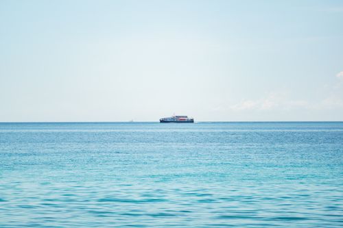 Free A serene view of a calm ocean with a ferry on the horizon under a clear blue sky. Stock Photo