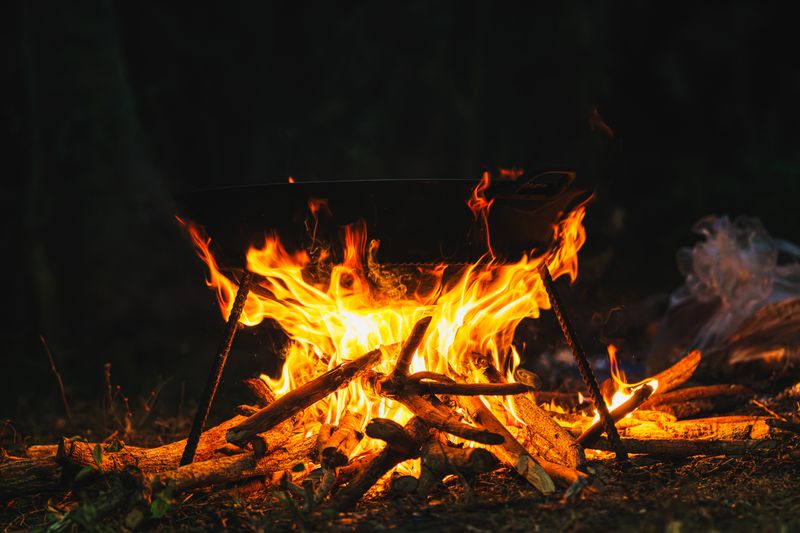 Cook pot over an open campfire after dark — photo by Nothing Ahead on Pexels