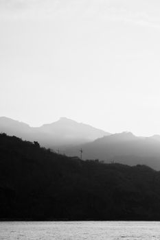 Black and white image depicting a tranquil mountain landscape with mist and sky.