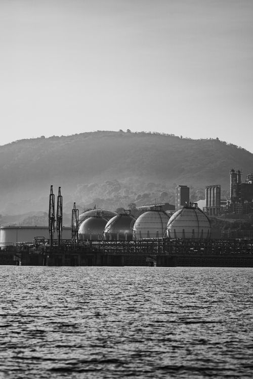 Free Black and white photo of spherical tanks and industrial plant near water with hill backdrop. Stock Photo